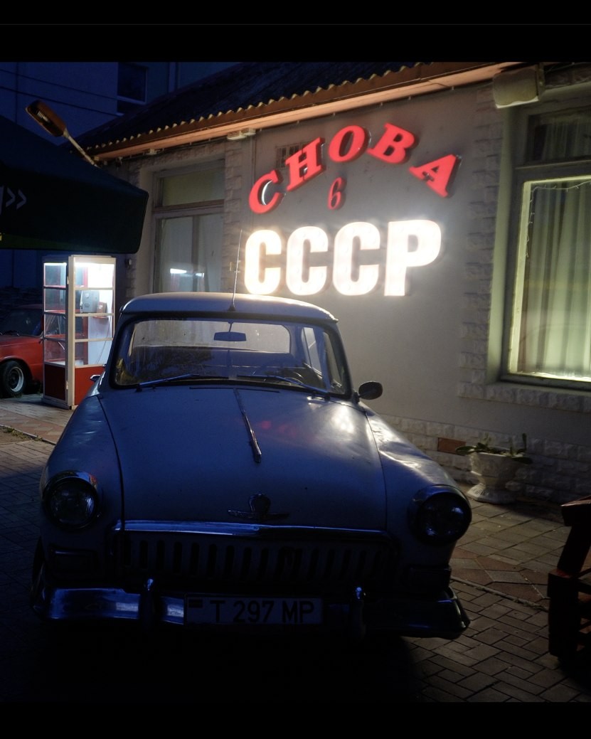 Samurai in Transnistria still — a vintage car parked outside a shop lit by a 'Снова СССР' neon sign at night